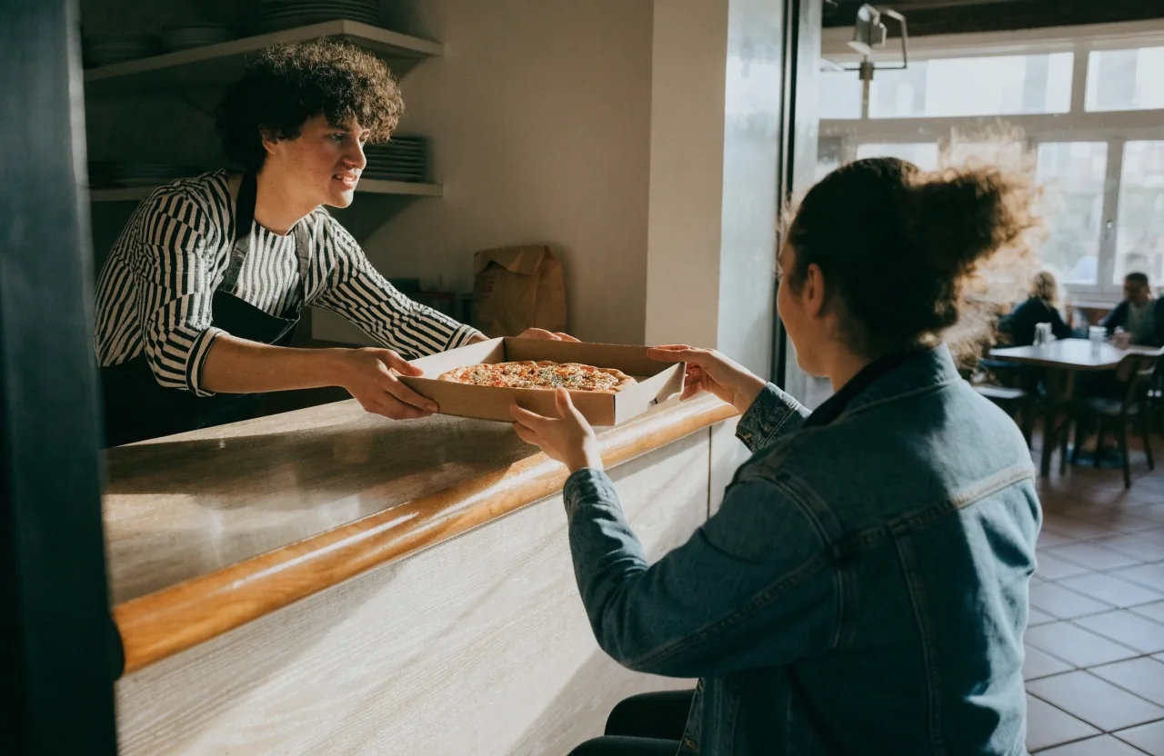 Team member handing a pizza box to a guest at the counter